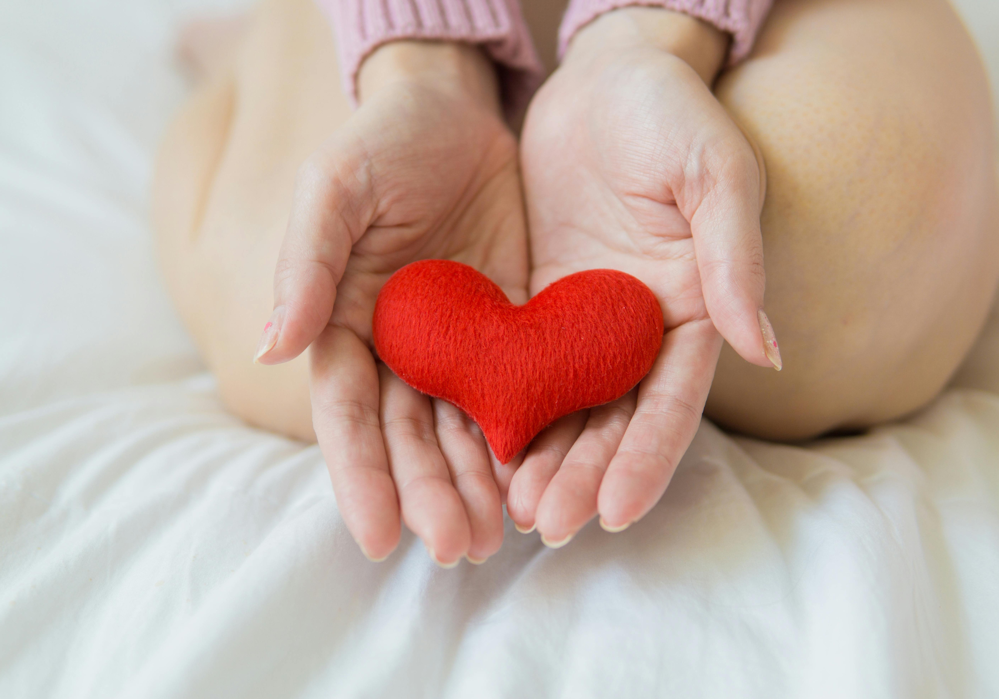 Hands holding a red heart-shaped object on a white background