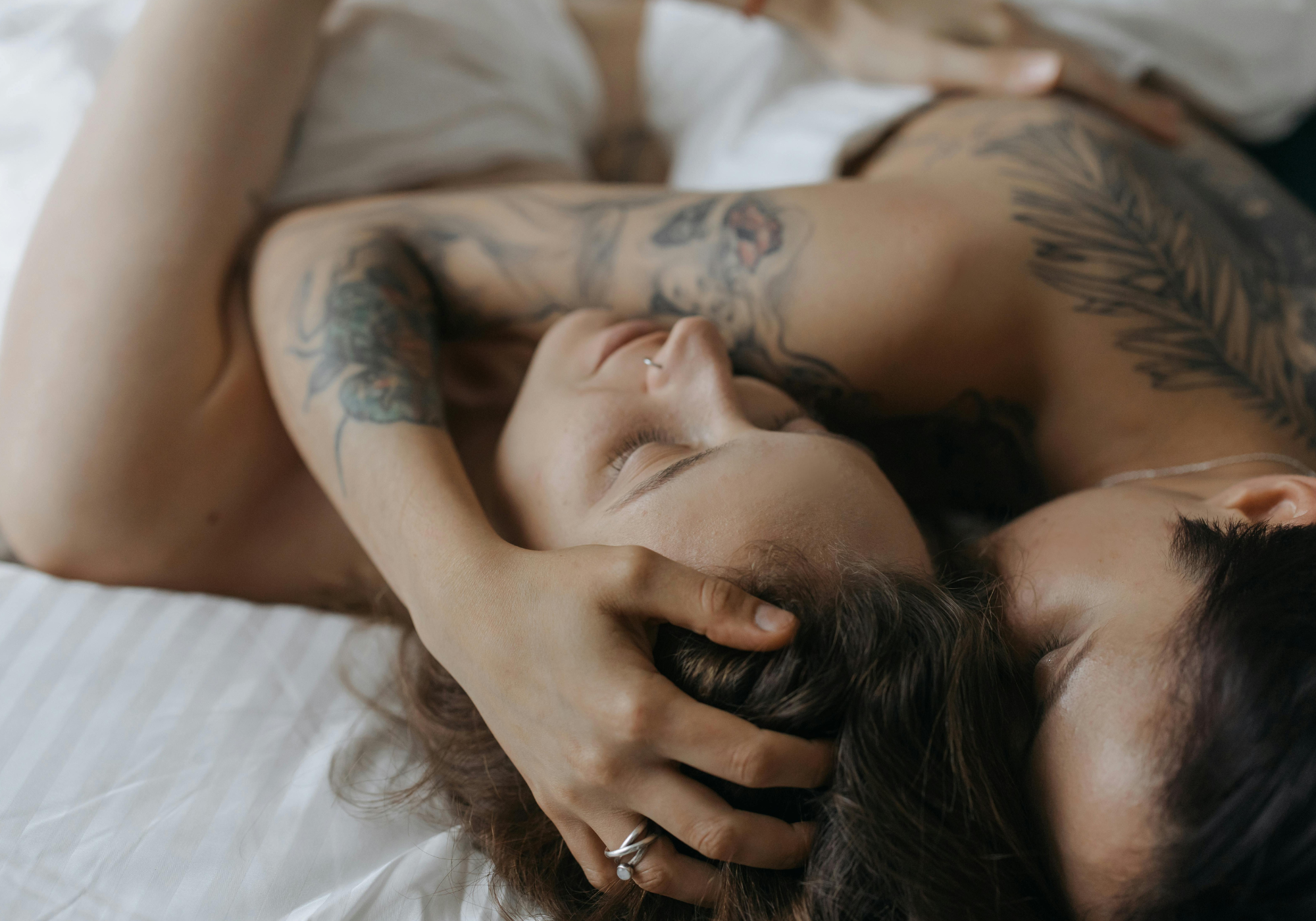 Two people lying close together on a bed with visible tattoos.