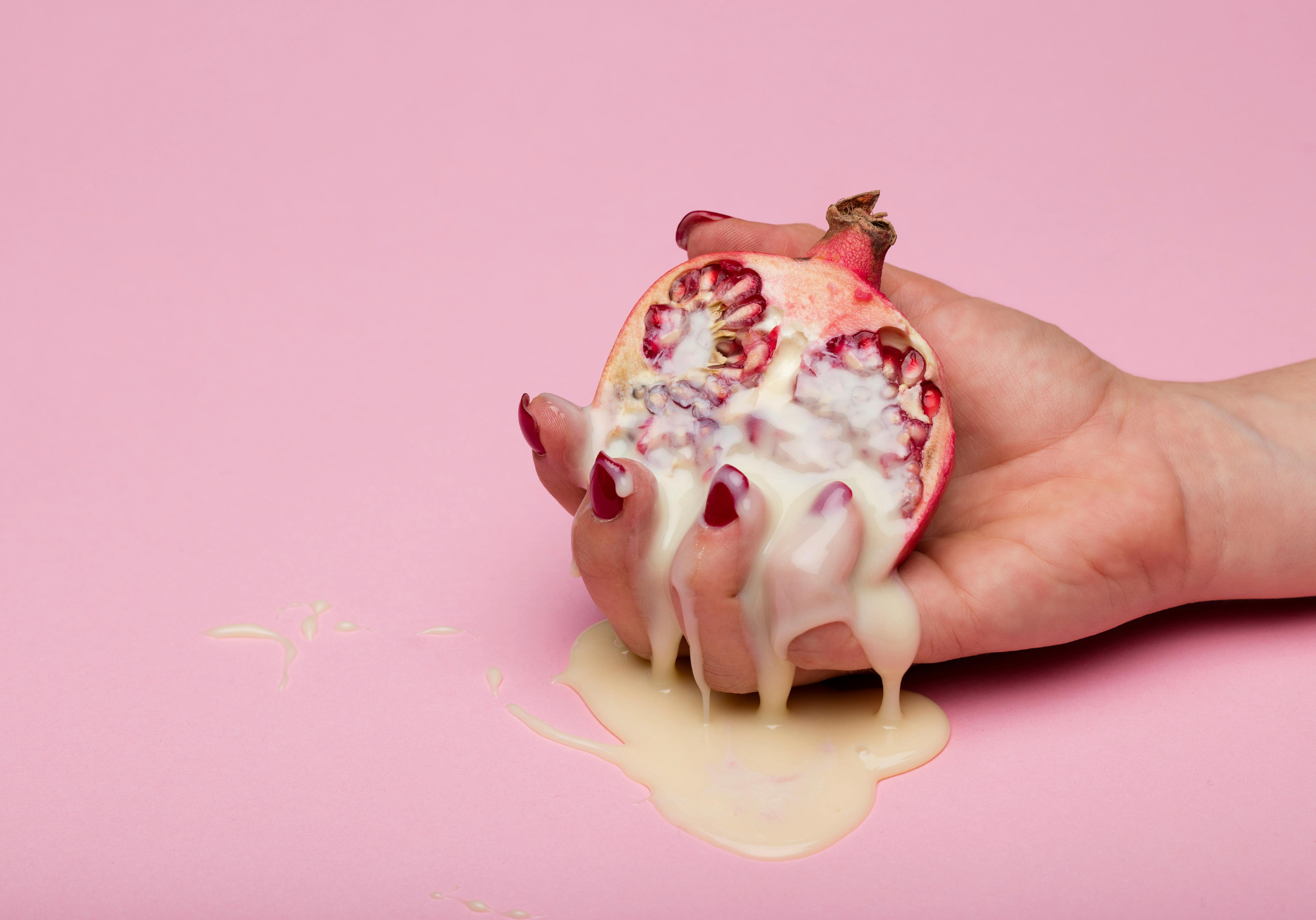 Hand holding a pomegranate with white liquid on a pink background