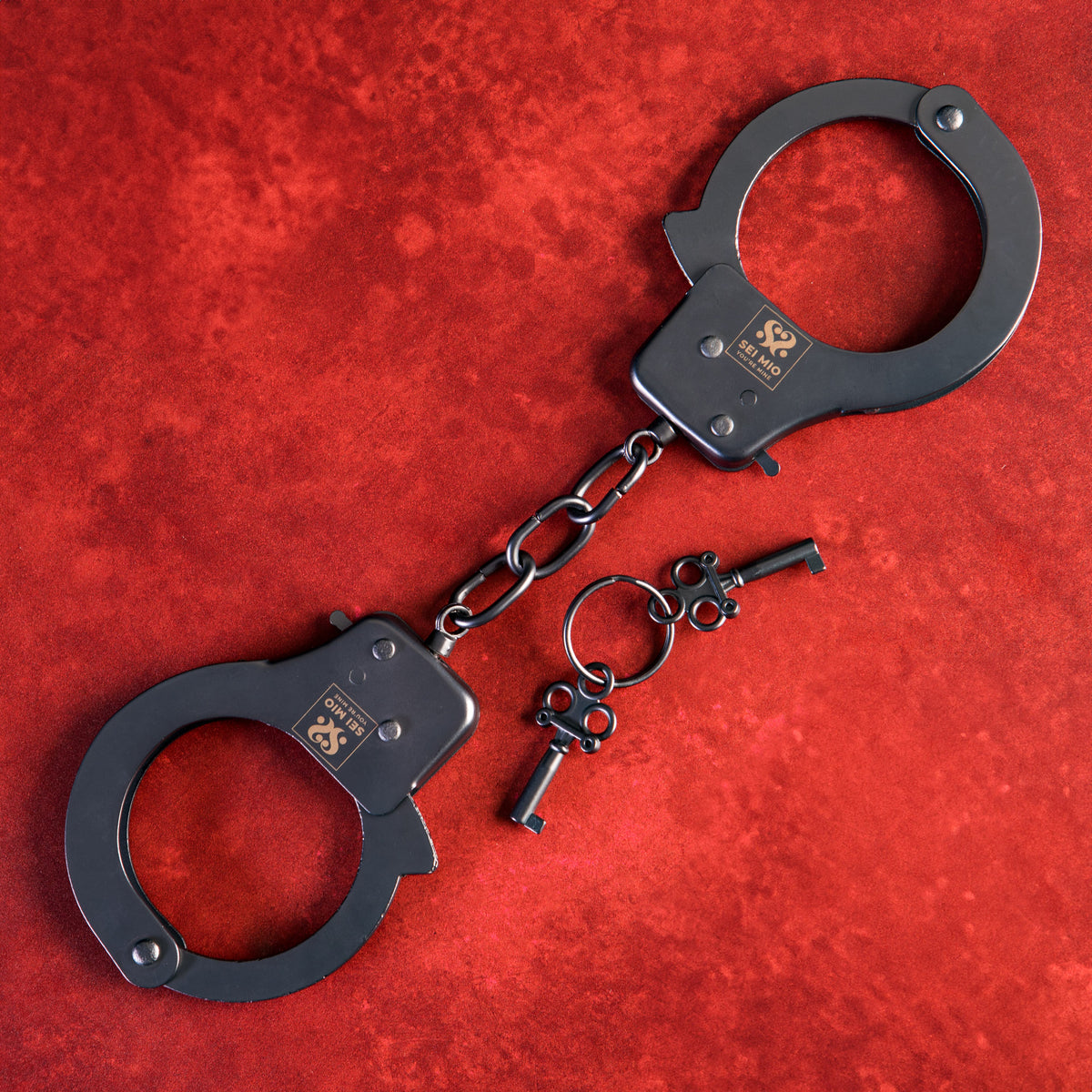 Sei Mio Secure and Begging for Amore metal handcuffs laid flat on red with two keys on a ring