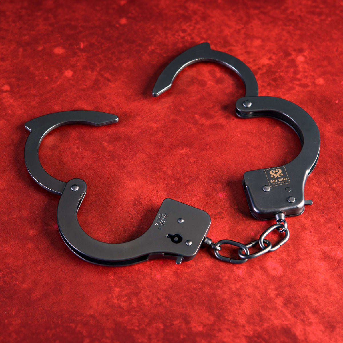 Sei Mio metal handcuffs shown open on a red background, displaying the cuffs and chain
