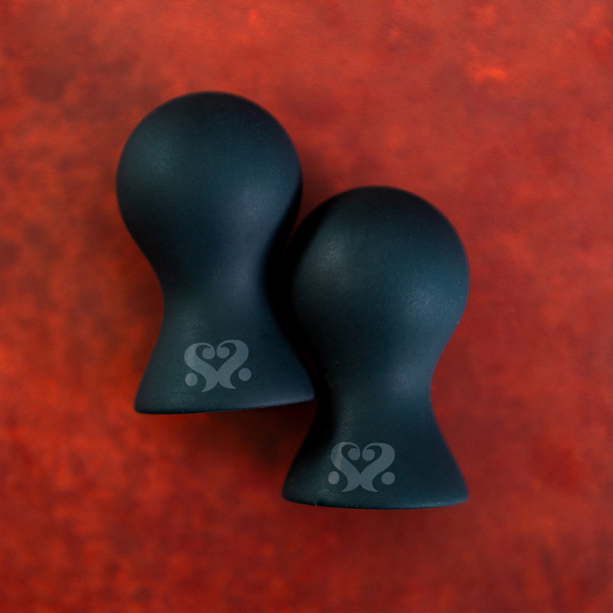 Pair of black Sei Mio Areola Grande silicone nipple suckers on a red background