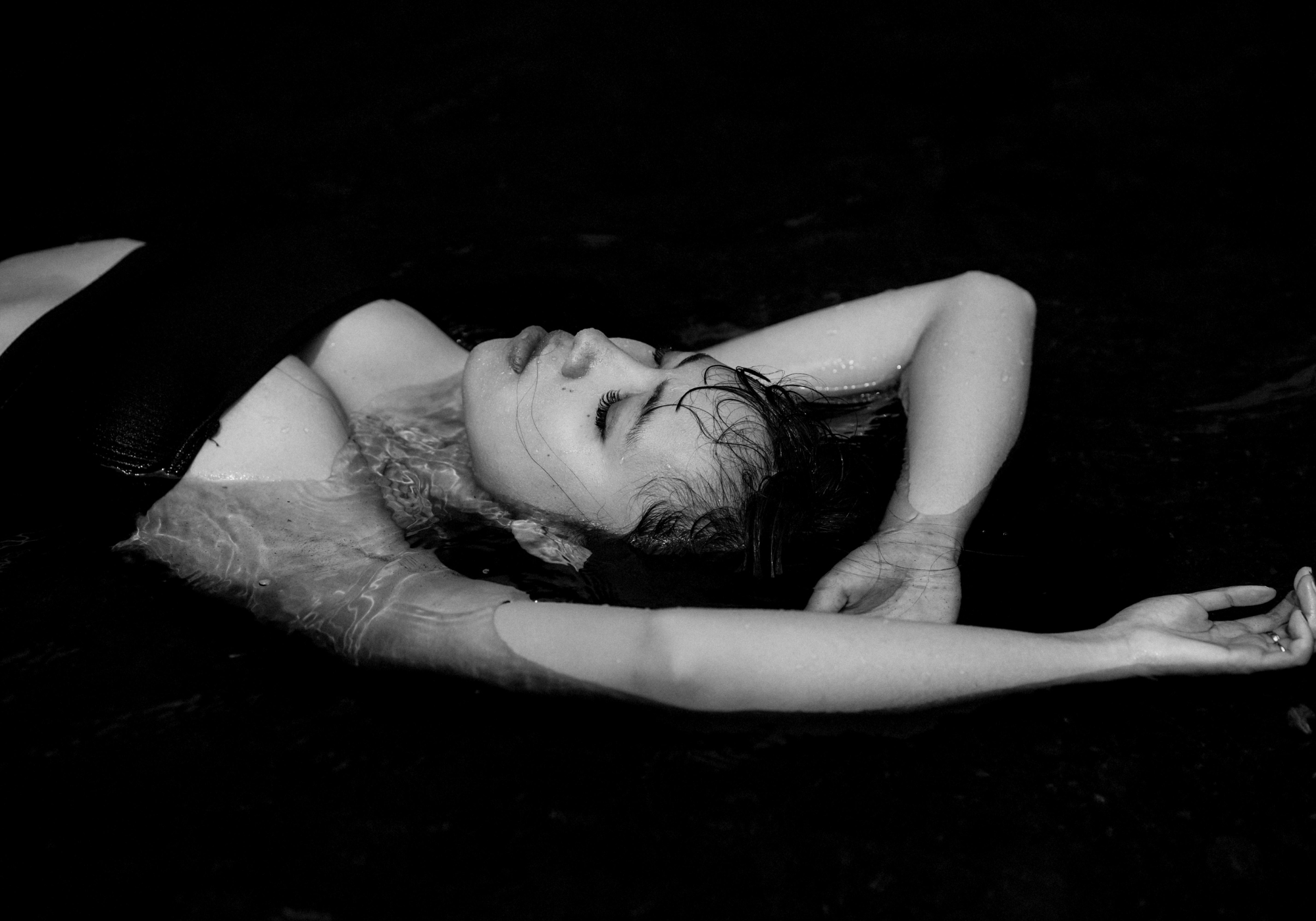Black and white photo of a person lying on a dark surface with minimal background