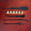 Sei Mio Correction Collection on red: spanking paddle, bamboo ruler, flogger, stinger, crop and two dice