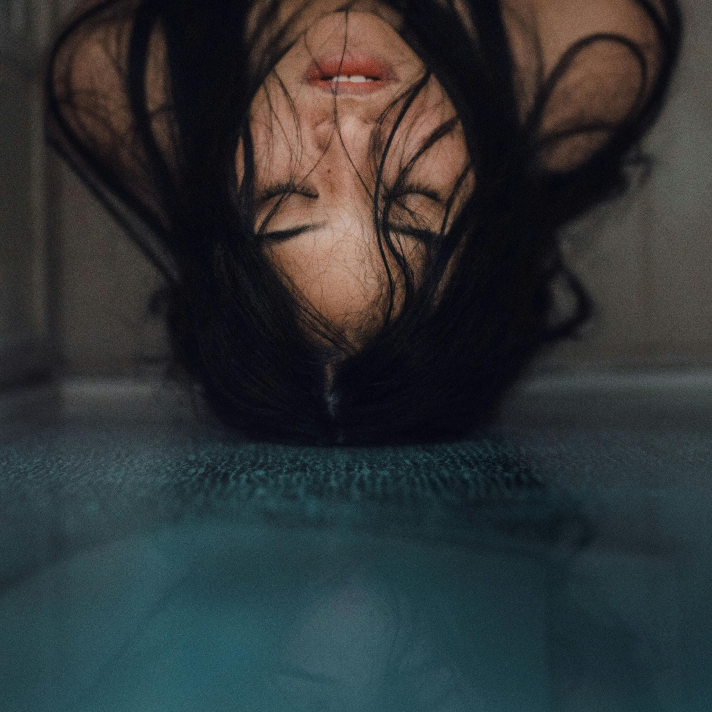 Person with dark hair covering their face, lying on a textured surface.