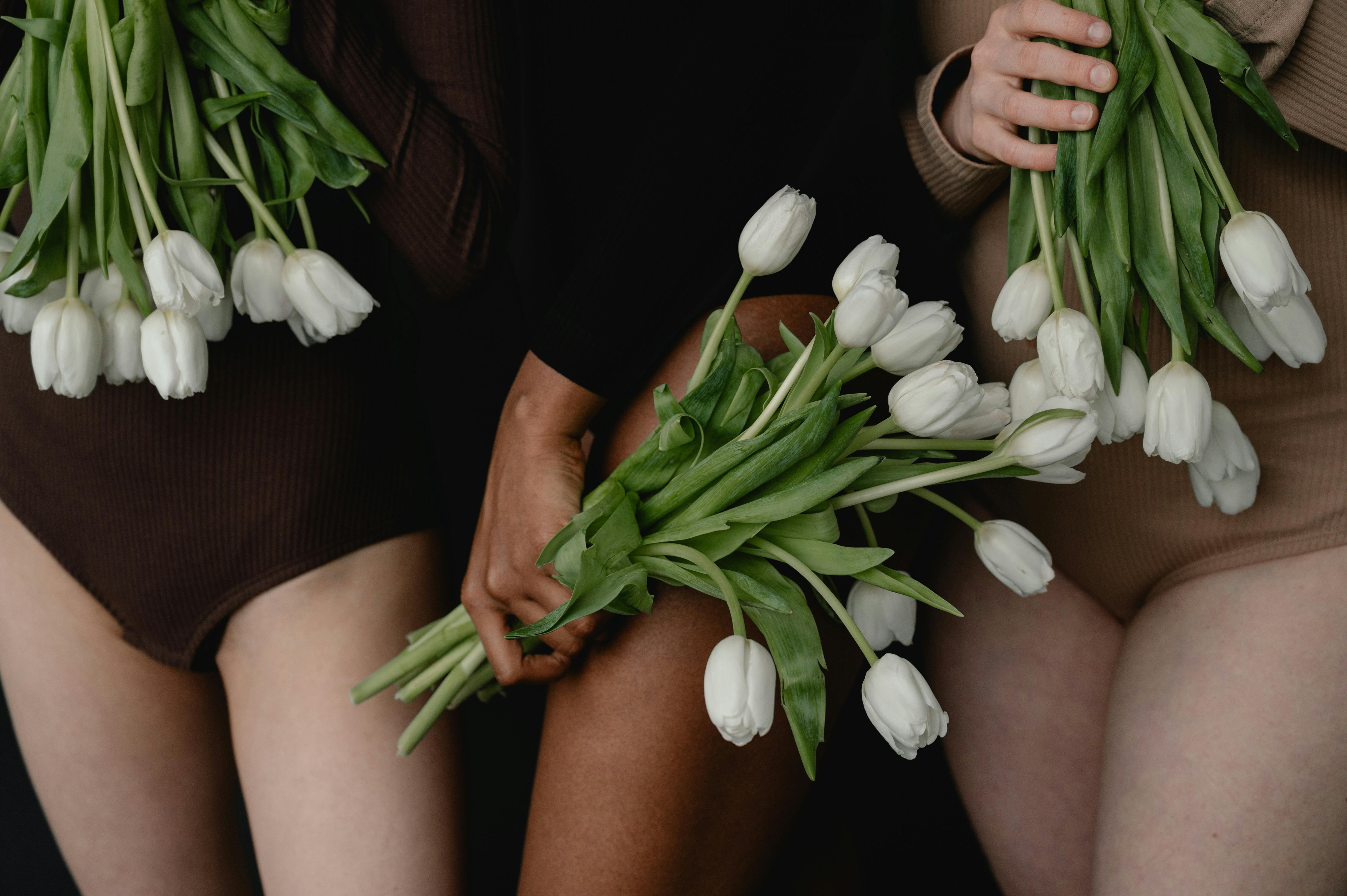 Two people holding white tulips in a dark setting
