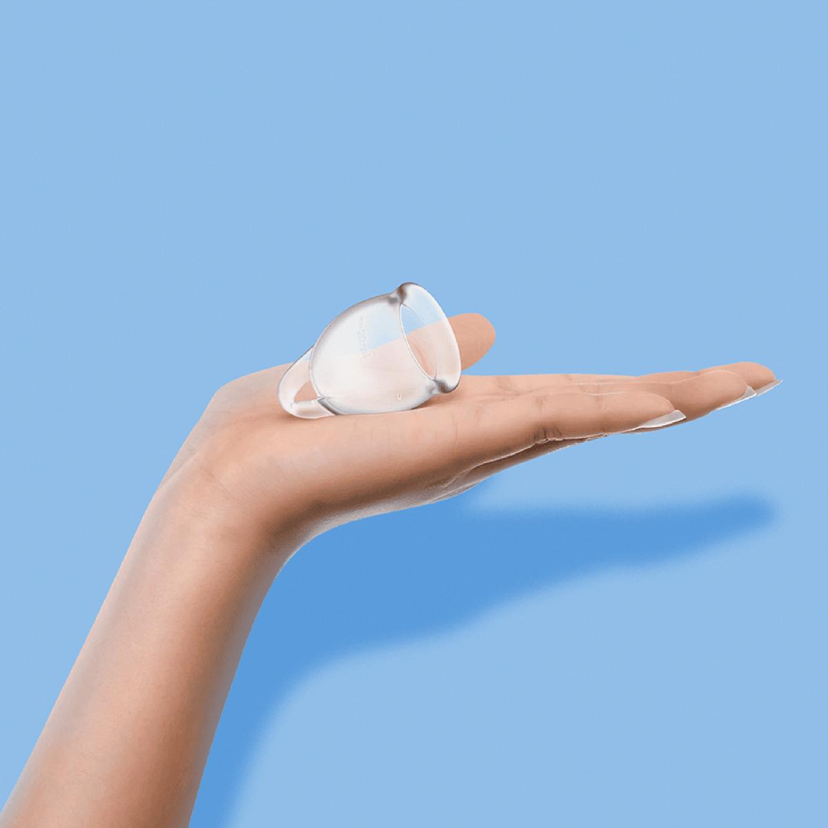 Satisfyer Feel Confident clear menstrual cup held in an open palm to show its size