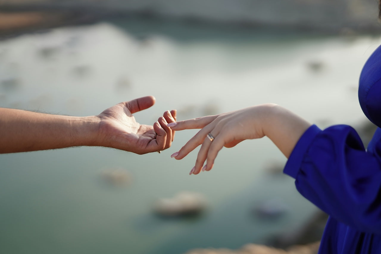 Two hands reaching towards each other with a blurred natural background