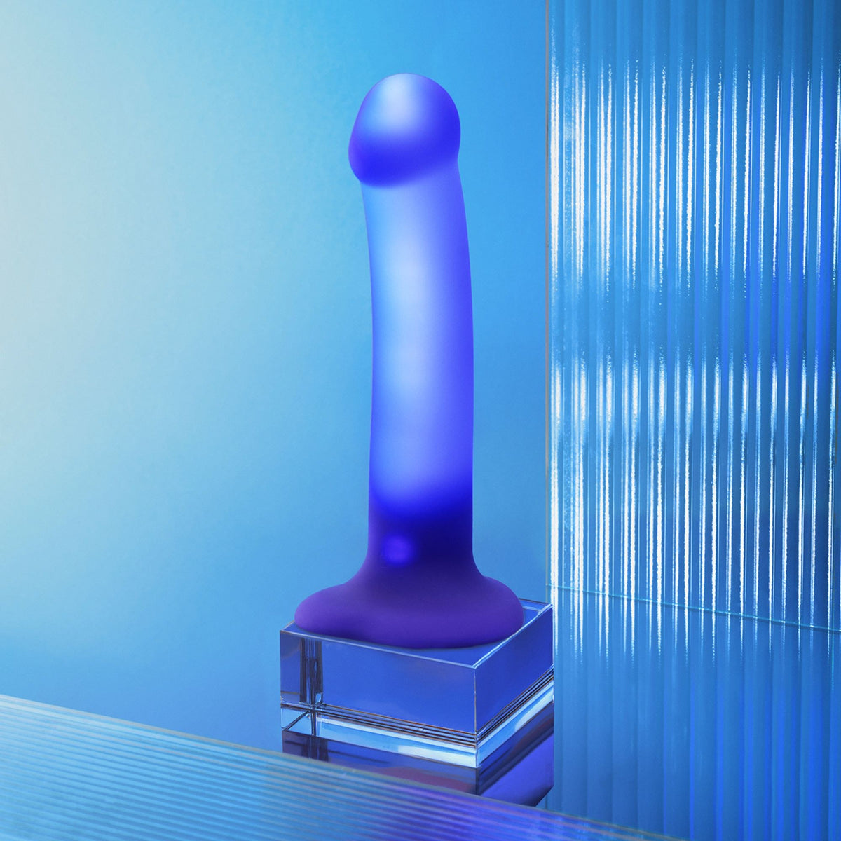 Strap On Me Glow LED Dildo in Purple, glowing on a glass block